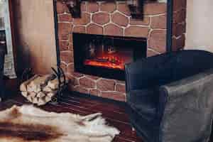 Бесплатное фото Вид на камин с горящими поленьями, натуральный мех на полу рядом с подставкой для поленьев в уютной комнате.