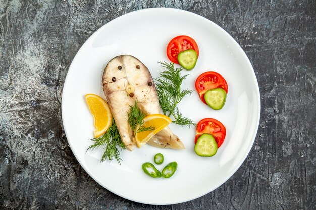 Above view of raw fishes and pepper fresh foods on white plate on gray ice surface with free space