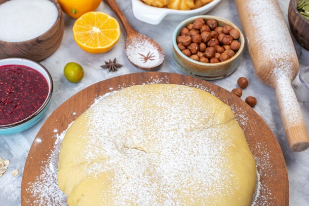 Above view of raw pastry flour on round board jam hazelnuts lemon slices grater on gray background