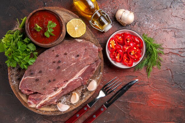 Above view of red meat on wooden tray and garlic green ketchup and chopped pepper oil bottle on dark background