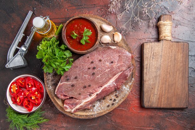 Above view of red meat on wooden tray and garlic green ketchup and chopped pepper oil bottle on dark background