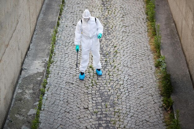 Above view of sanitation worker in protective suit spraying city streets with disinfectant during COVID19 epidemic