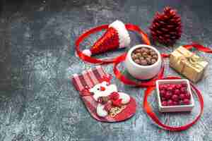 Free photo above view of santa claus hat and cornel chocolate new year sock red conifer cone on the left side on dark surface