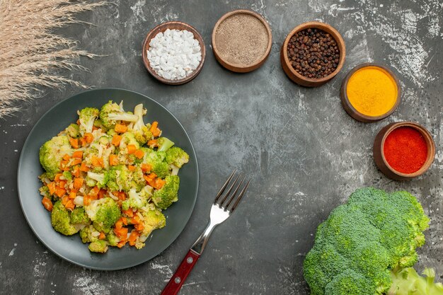 Above view of set of different spices in brown bowls and vegetable salad with fresh broccoli