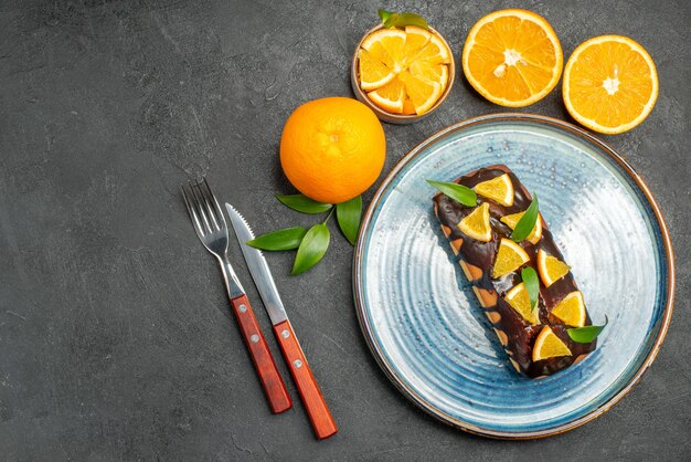 Above view of set of yellow whole and cut oranges tasty cakes on dark table