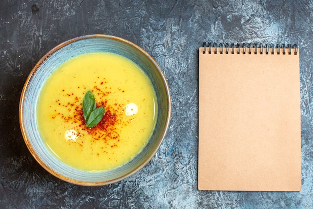 Above view of spiral notebook and a blue pot with tasty soup on blue table