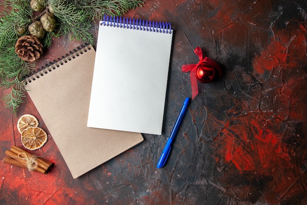 Above view of spiral notebooks and pen fir branche cinnamon limes conifer cone on dark background