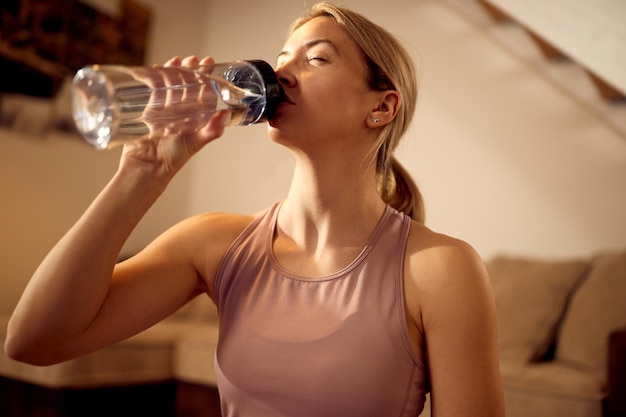 Free photo below view of sportswoman drinking water while exercising at home