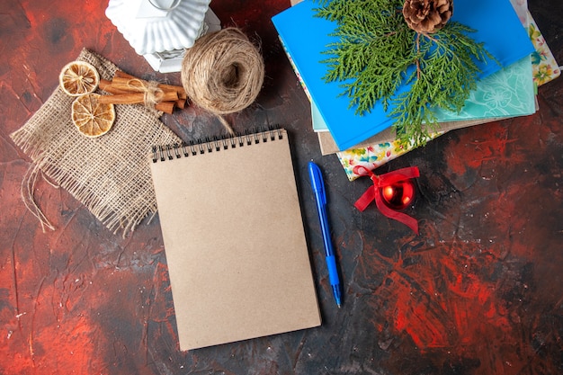 Above view of stacked notebooks and pen ball of rope cinnamon limes conifer cones on dark background