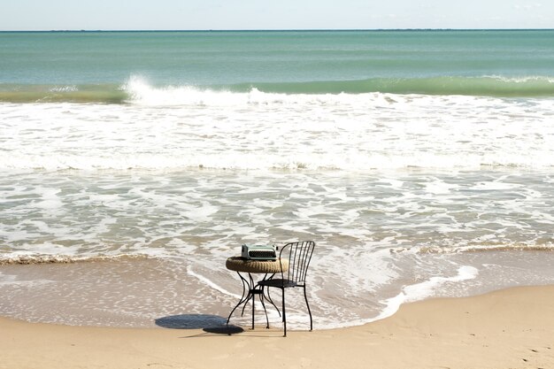 View of a steel chair and a small round table on a sandy shore with waves