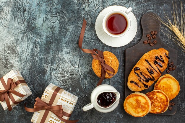 Above view of tasty breakfast with pancakes croisasant stacked cookies gift boxes on dark table