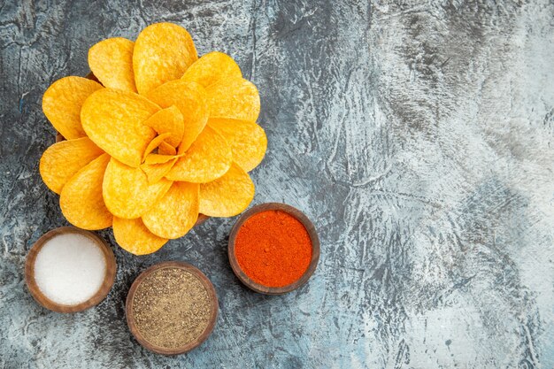 Above view of tasty potato chips decorated like flower shaped and different spices on gray table