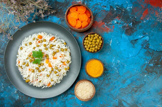 Above view of tasty rice meal for dinner with pisum carrot on purple stripped towel and its ingredients on blue table