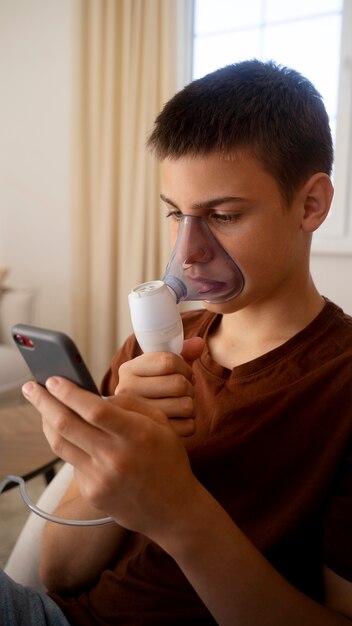呼吸器系の健康上の問題のために自宅でネブライザーを使用している 10 代の少年の様子