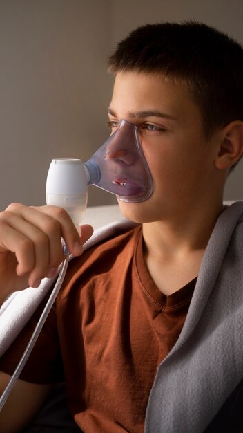 View of teenage boy using nebulizer at home for respiratory health problems