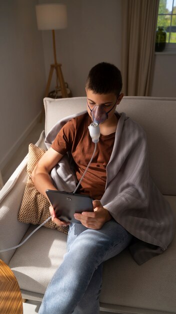 View of teenage boy using nebulizer at home for respiratory health problems