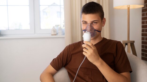View of teenage boy using nebulizer at home for respiratory health problems