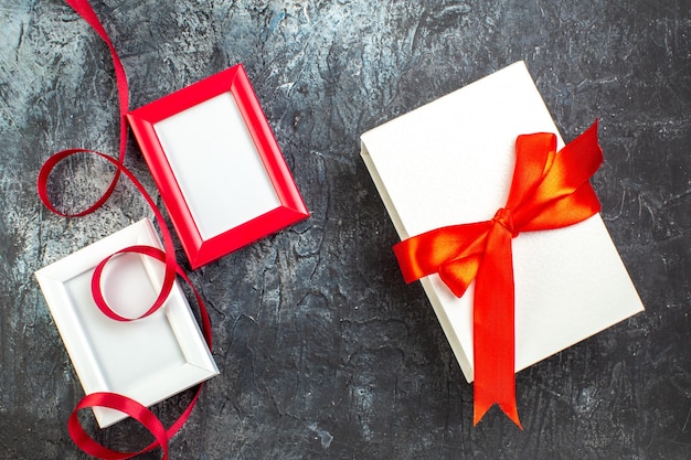 Above view of three empty picture frames and gift with ribbon on dark