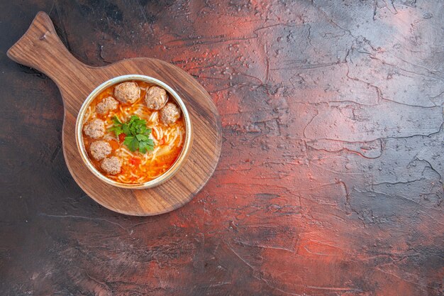 Выше вид томатного супа с фрикадельками с лапшой в коричневой миске на темном фоне