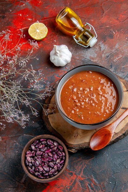 Above view of tomato soup in a blue bowl on a tray beans oil bottle on mixed color table