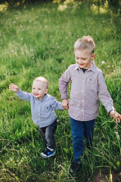 View of two little happy brothers wearing jeans and checked shirts walking playing in park going forward Boys wearing among green grass running and happy smiling Concept of kids fashion