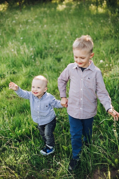 ジーンズとチェックのシャツを着て、公園で遊んで歩いている2人の小さな幸せな兄弟の様子緑の芝生の中で走っている男の子と幸せな笑顔キッズファッションのコンセプト