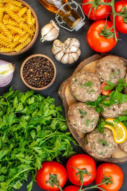 Above view of uncooked meatballs on a wooden cutting board and fresh vegetables green on dark background