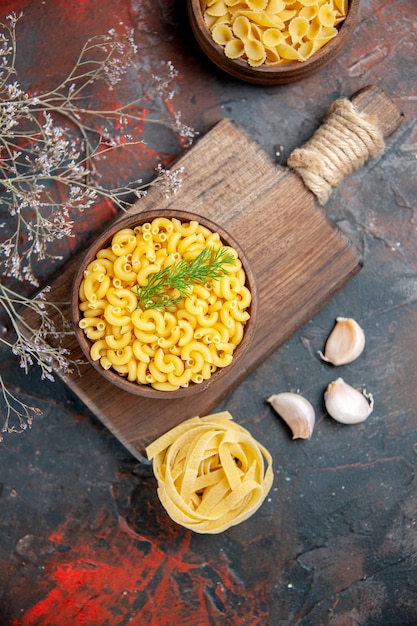 Foto gratuita sopra la vista di pasta cruda in una ciotola marrone e aglio sul tagliere di legno sul tavolo di colori misti