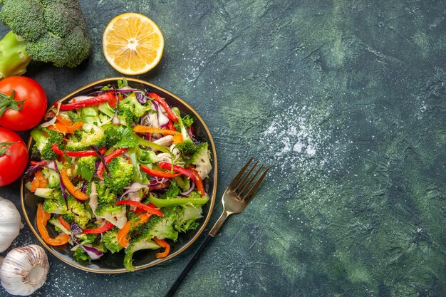 Above view of vegan salad in a plate and fresh vegetables on dark background