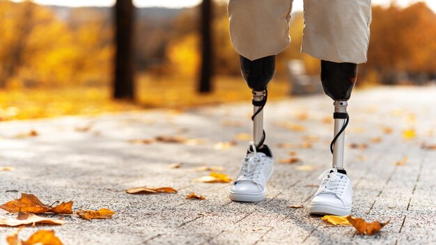 Вид на идущего человека с протезами ног и белыми кроссовками Павшие желтые листья на земле