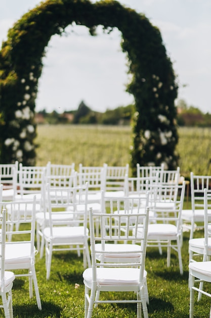 view on white chairs and archway before wedding ceremony