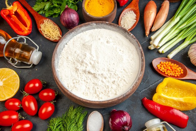 Above view of white flour in a brown pot fresh vegetables eggs different spices on dark