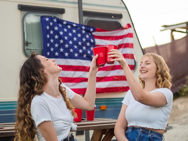 View of white girls clinking cups with the flag of the United States of America in the background