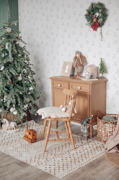 View over white modern room decorated for Christmas holidays. Decorated and illuminated Christmas tree, fireplace with fir branch, candles and handmade paper stars in fireplace.