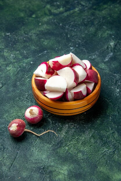 Above view of whole and chopped fresh radishes inside and outside of a wooden bowl on dark color background with free space