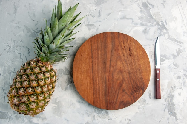 Above view of whole fresh golden pineapple and cutting board knife on table on marble surface