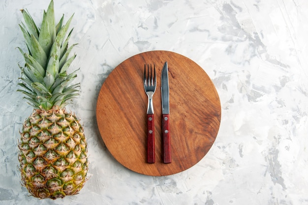 Sopra la vista dell'intero coltello forchetta d'ananas dorato fresco sul tagliere su superficie di marmo