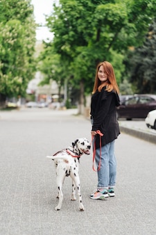 Vista di una giovane donna caucasica che cammina in città durante la mattinata con un cane dalmata