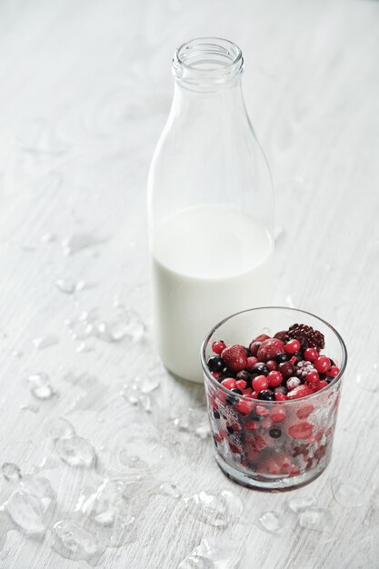 Vintage bottle with milk near glass with frozen berries ready for cocktail making isolated on white table with melted ice