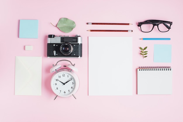 Free photo vintage camera; alarm clock and stationeries on pink background