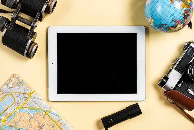 Vintage camera; binocular; globe; map; flashlight near the digital tablet on beige background