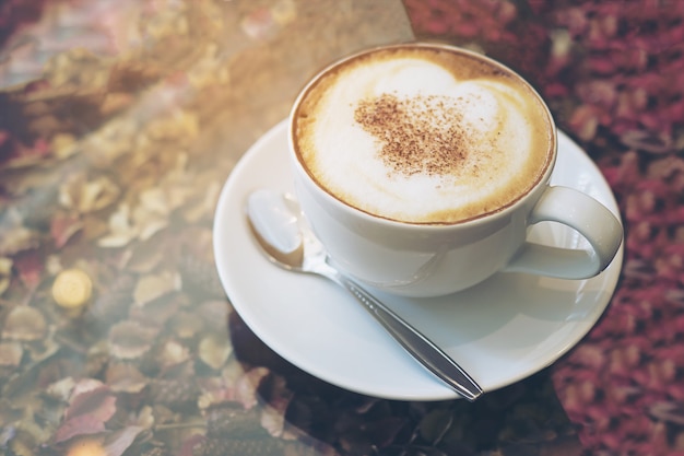 Vintage picture of hot coffee cup on dry flower petals texture and glass table top