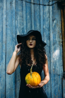 Vintage woman as witch posing with pumpkin in the hands against abandoned place on the eve of halloween