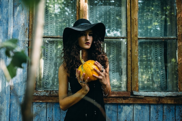 Vintage donna come strega in posa con la zucca nelle mani contro il luogo abbandonato alla vigilia di halloween