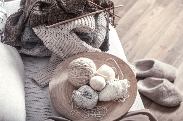 Vintage wooden knitting needles and threads on a cozy sofa with pillows and Slippers nearby