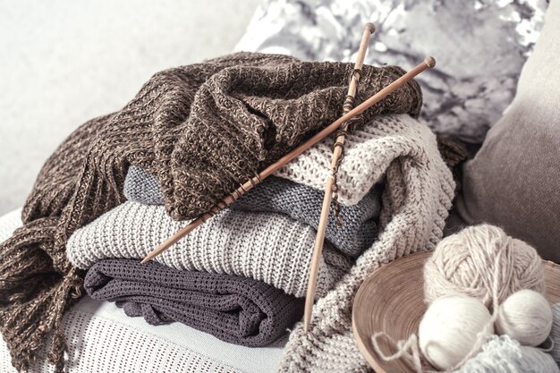 Vintage wooden knitting needles and threads for knitting on a cozy sofa with pillows and sweaters