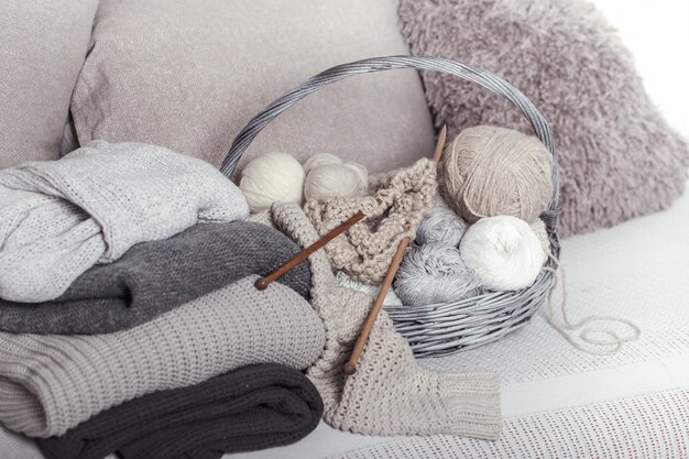 Vintage wooden knitting needles and threads in a large basket on a cozy sofa with sweaters. Still life photo