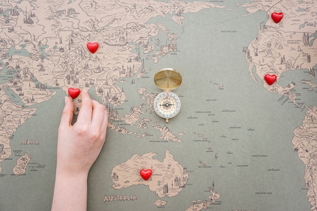 Vintage world map background with compass and hand placing red hearts