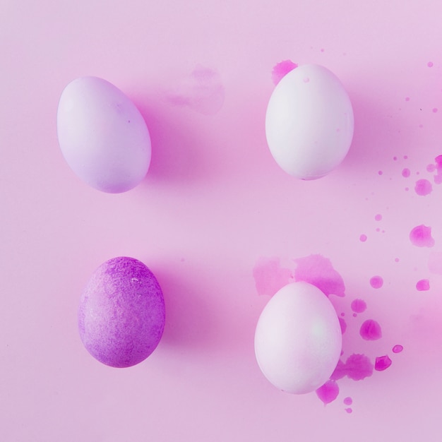 Фиолетовые и белые пасхальные яйца между брызгами красителя жидкости
