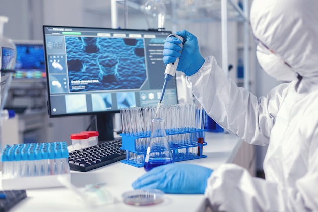 Virolog coducting experiment in the course of coronavirus pandemic with micropipette. Chemist in modern laboratory doing research using dispenser during global epidemic with covid-19.